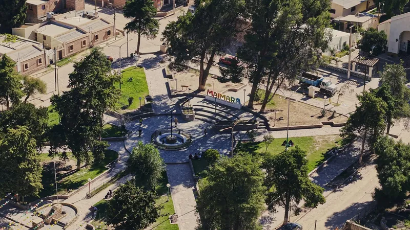 Vista aérea de la plaza con la fuente central, el cartel de colores de Maimará y los árboles que la rodean.